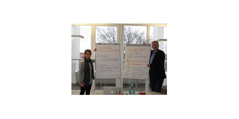 Zwei Personen stehen neben Flipcharts und präsentieren ihre erarbeiteten Ergebnisse
