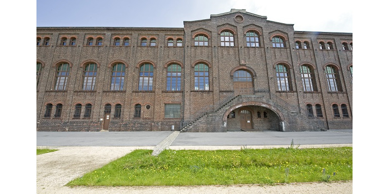 Ansicht eines Gebäudes aus Backstein mit Rasenstreifen im Vordergrund: Das Industriedenkmal Maschinenhalle Zweckel.