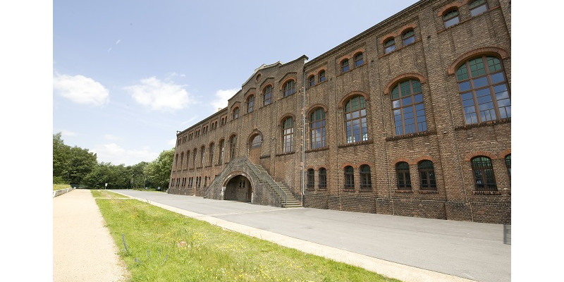 Ansicht eines Gebäudes aus Backstein mit Rasenstreifen im Vordergrund. Das Industriedenkmal Maschinenhalle Zweckel.