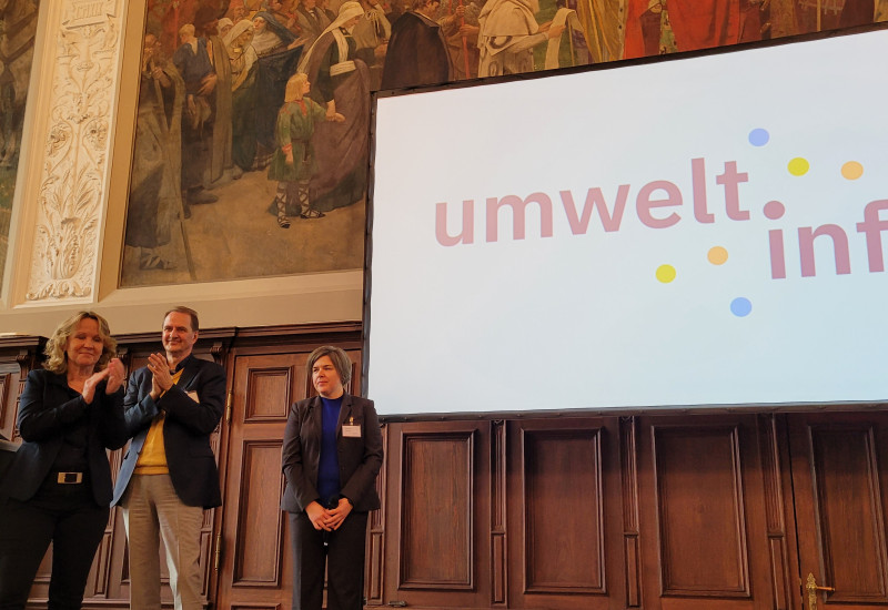 Bundesumweltministerin Steffi Lemke, UBA-Präsident Dirk Messner und xyz stehen vor einer Leinwand mit dem Logo des Portals umwelt.info.