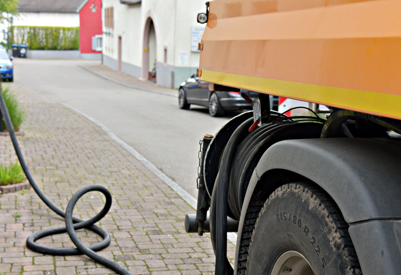 Ein Lastwagen steht am Straßenrand und pumpt über einen schwarzen Schlauch Öl in den Keller eines Hauses.