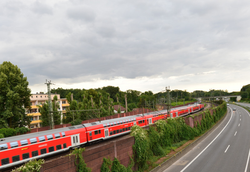Fahrender Zug neben Bundesstraße nahe einem Wohngebiet