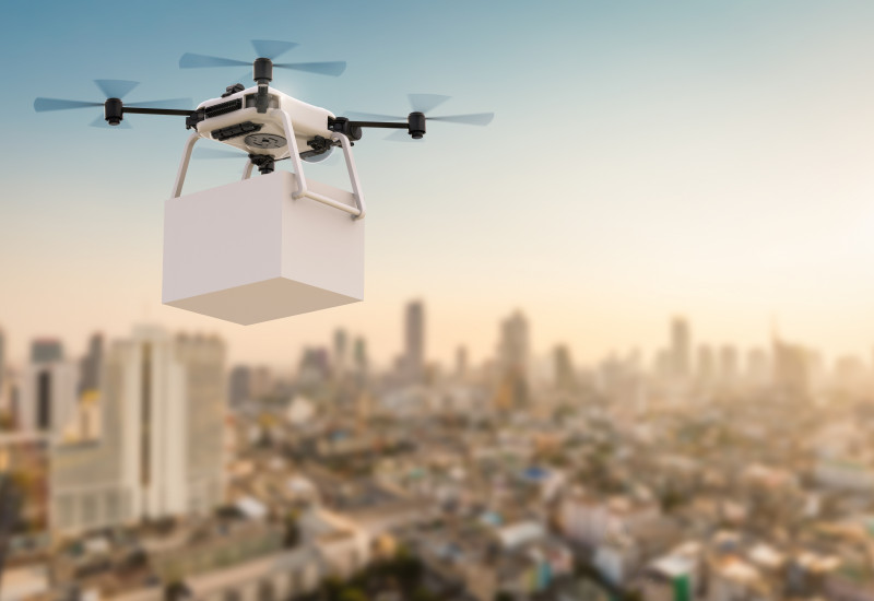 Eine Drohne, die mit einem Paket über einer Stadt fliegt.