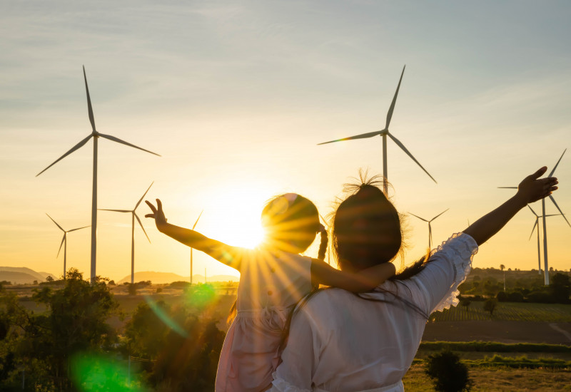 Menschen winken vor Windrädern im Sonnenschein