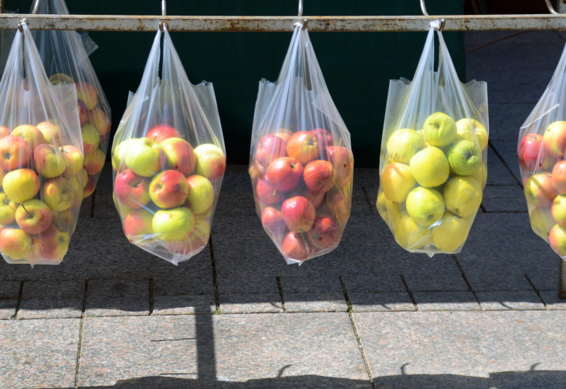 an einer Eisenstange über einem gepflasterten Platz oder Fußweg hängen durchsichtige Plastiktüten mit Äpfeln