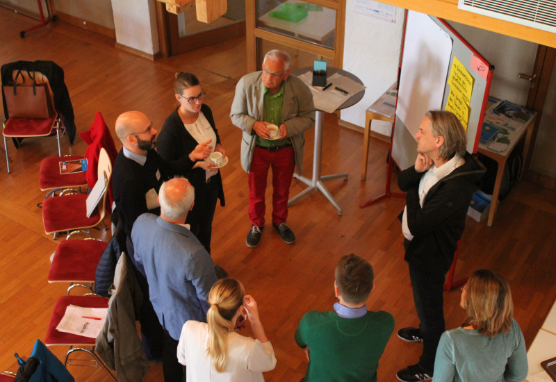 eine Gruppe von Menschen steht um eine Flipchart und diskutiert 