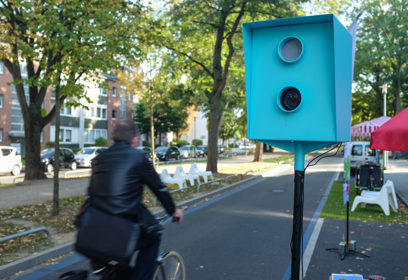 Radfahrer passiert "Fotokasten" der Bilder zum Geburtstag der Blauen Route schießt