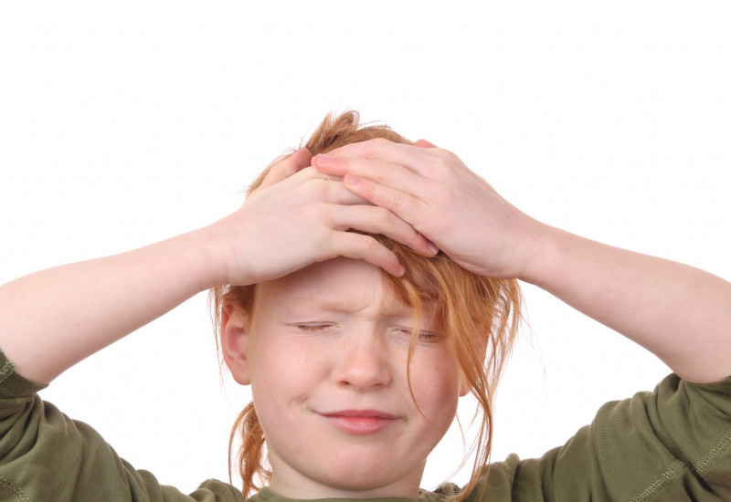Ein Kind, das sich schmerzverzerrt den Kopf mit beiden Händen hält.