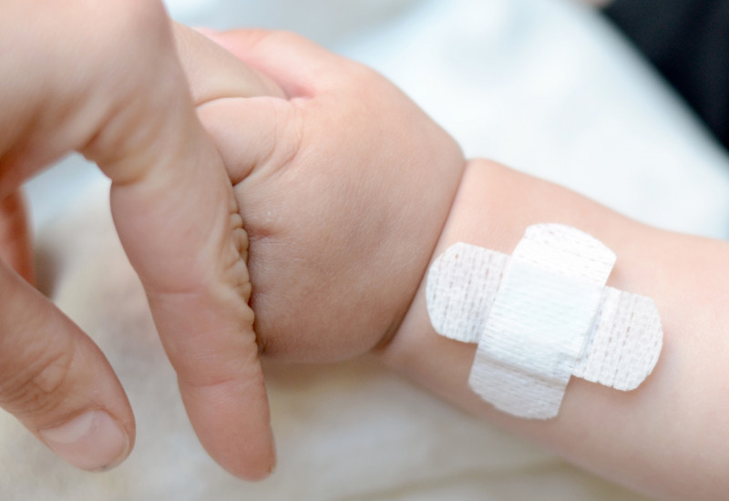 A baby hand holding the finger of an adult