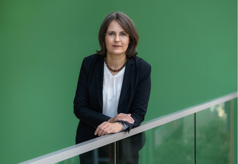 Dr. Claudia Röhl leaning on a stair railing in front of green background