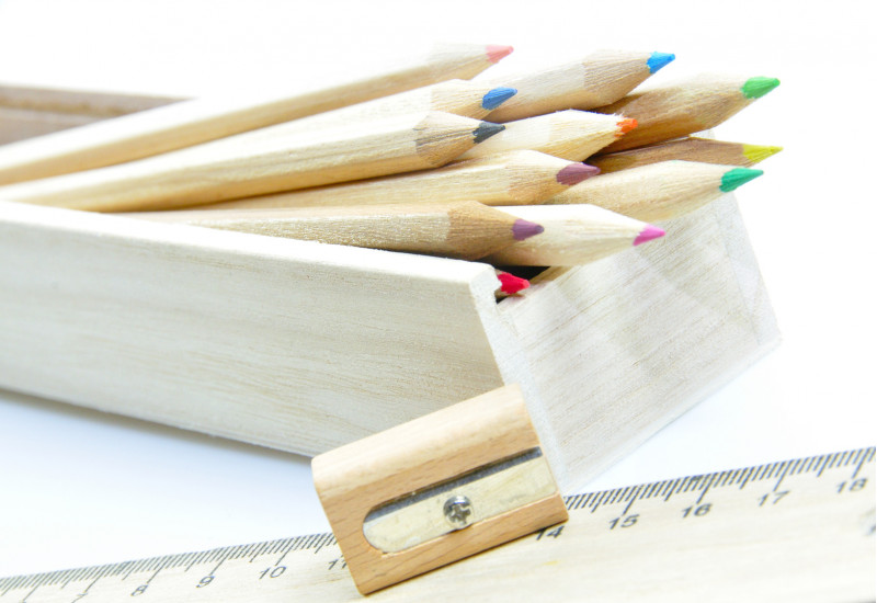 unlackierte Holz-Buntstifte in einem Holzkästchen, daneben ein Anspitzer aus Holz und ein Lineal