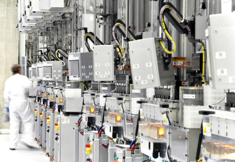 Arbeiter mit weißem Schutzanzug in der Werkhalle einer Chipfabrik mit vielen Geräten