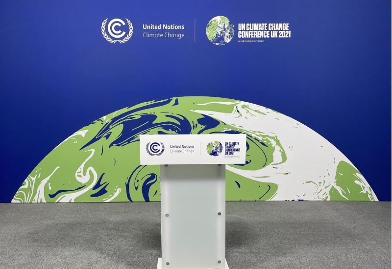 Rednerpult mit der Aufschrift "UN Climate Change Conference UK 2021", im Hintergrund eine Aufstellwand mit derselben Aufschrift und einer Erdkugel