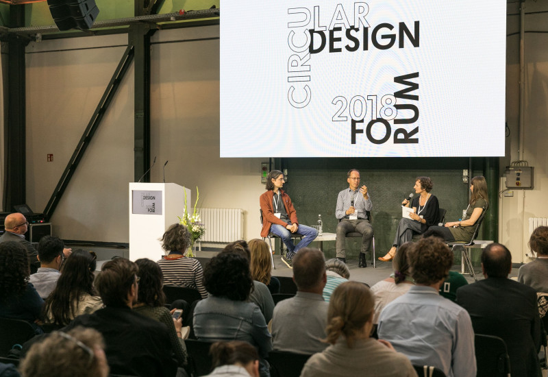 zwei Männer und zwei Frauen diskutieren mit Mikrofonen in einem Halbkreis sitzend auf einer Bühne vor Publikum, darüber ein Banner mit der Aufschrift "Circular Design Forum 2018"