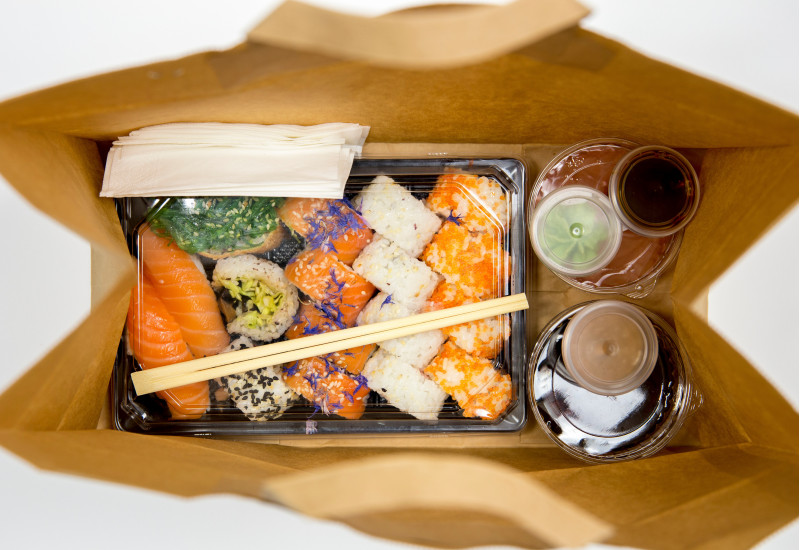 Sushi und mehrere Soßen alle einzeln in Einwegplastikbehältnissen verpackt in einer Papiertüte zum Mitnehmen
