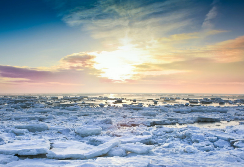 Eisschollen auf dem Meer, im Hintergrund färbt die tief stehende Sonne die Wolken am Horizont rosa