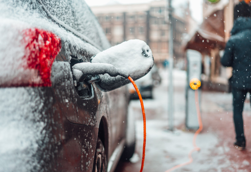 Ein verschneites Elektroauto wird  bei winterlichen Bedingungen geladen.