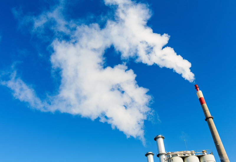 rauchende Schornsteine einer Industrieanlage vor blauem Himmel
