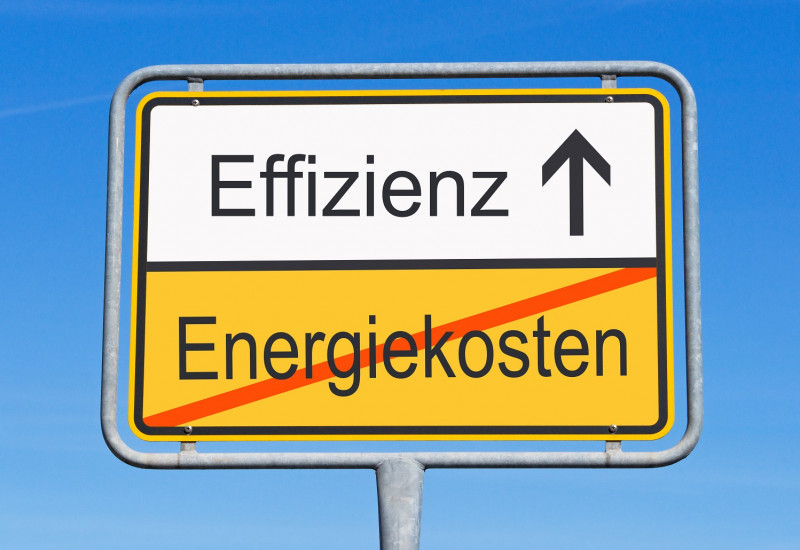 ein gelbes Ortsschild weist den Weg hin zu "Effizienz", darunter ist der Schriftzug "Energiekosten" durchgestrichen