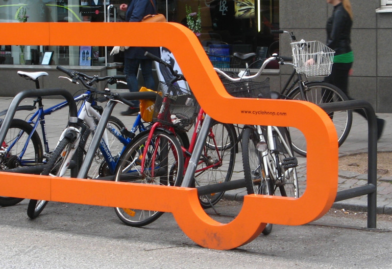 an der Front eines Fahrradständers für mehrere Räder in der Stadt ist ein lebensgroßer Umriss eines Autos angebracht und verdeutlicht: wo sonst nur ein Auto hinpasst, passen viele Fahrräder hin
