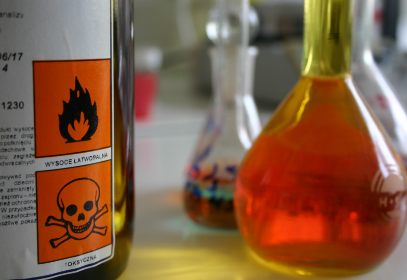 auf einem Tisch stehen Flacons mit Flüssigkeiten und eine Flasche mit Warnsymbolen "Flamme" und "Totenkopf"
