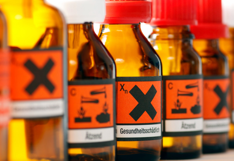 Glasfläschchen mit Warnhinweisen wie "ätzend" und "gesundheitsschädlich".