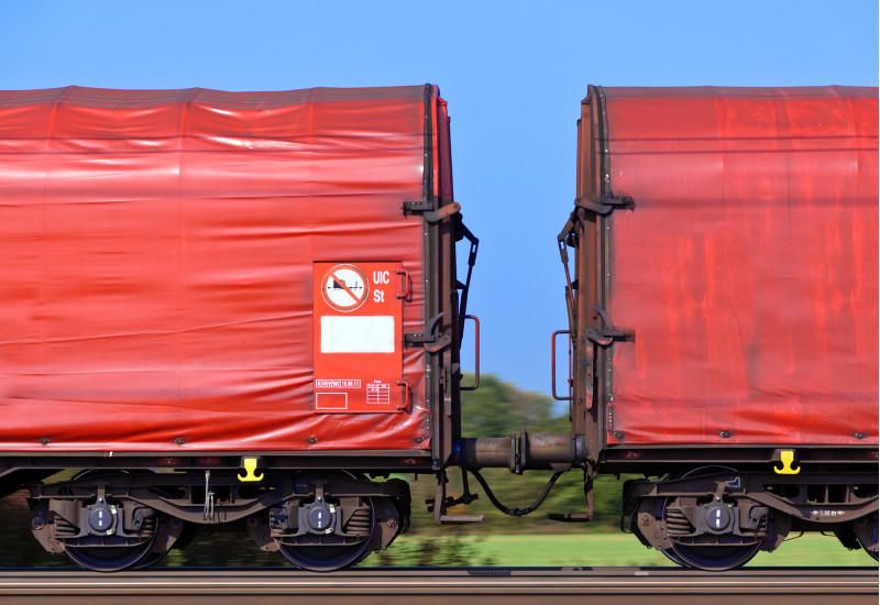 zwei rote Güter-Waggons auf der Schiene vor blauem Himmel und grüner Landschaft