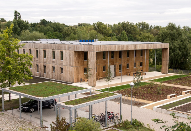 quadratischer zweigeschossiger Bau mit Holzfassade und Solarzellen auf dem Dach