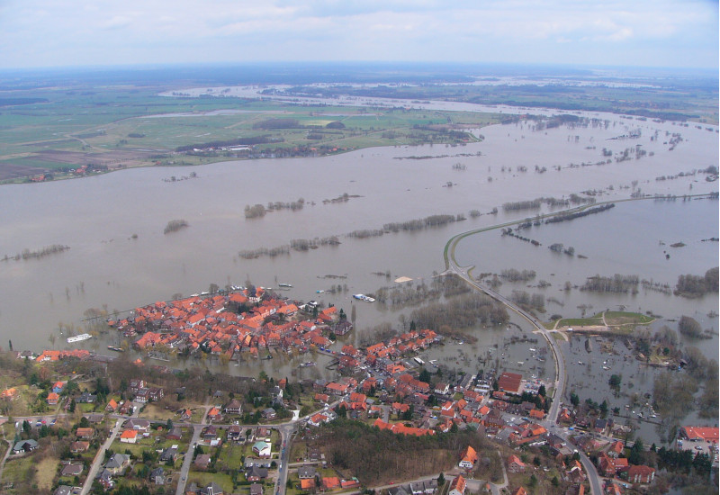 Luftbild: eine Landschaft mit einer Siedlung ist großflächig überschwemmt