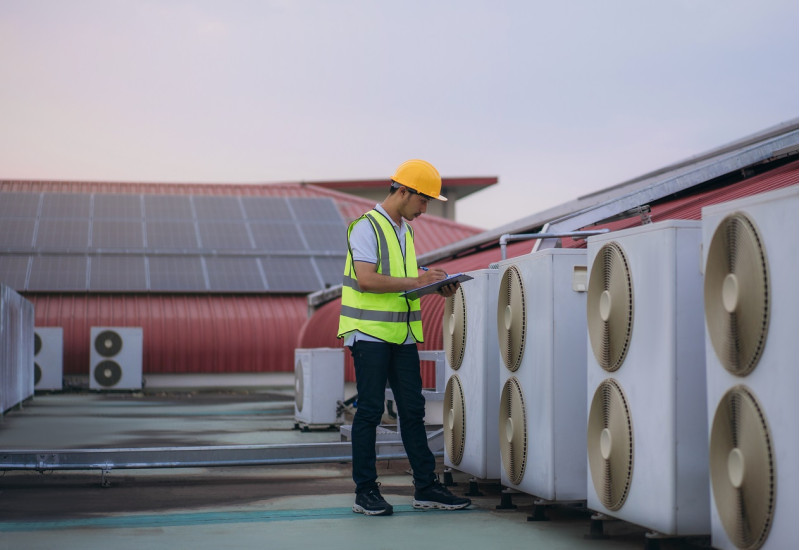 Mann in Arbeitskleidung kontrolliert Klimaanlagenaggregate auf einem Hausdach mit Photovoltaikanlage