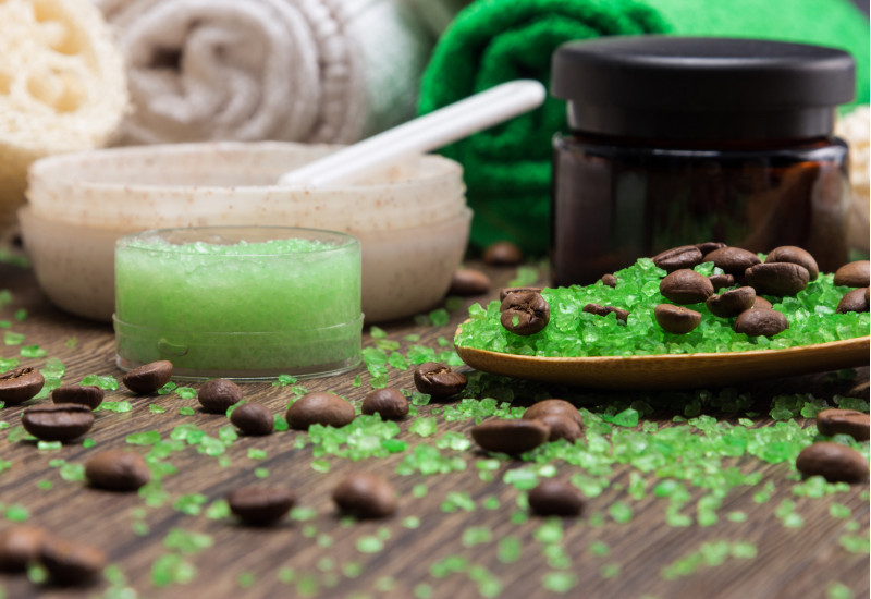 Kosmetiktiegel und Handtücher mit grünen Kügelchen und Kaffebohnen auf einer Holzoberfläche arrangiert