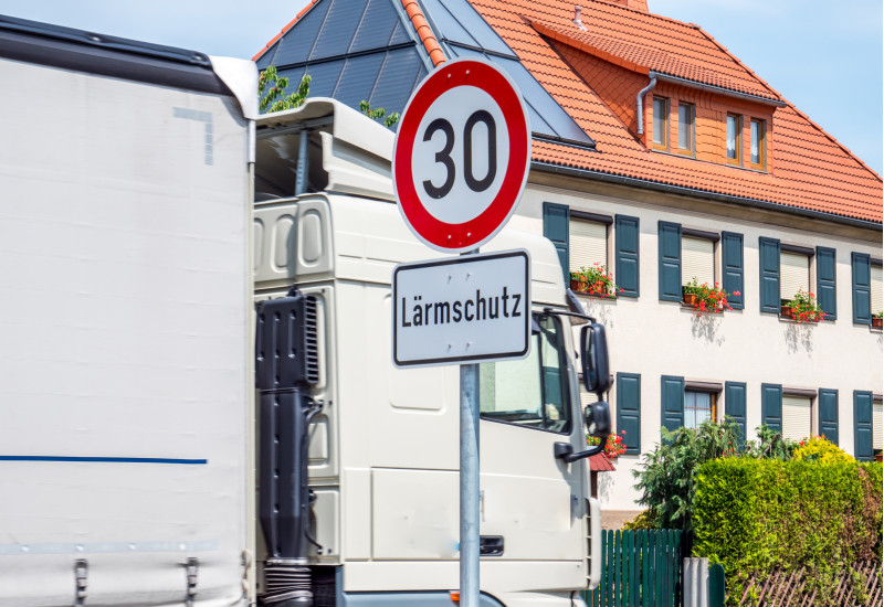 Ein Tempo 30-Schild mit Zusatzschild Lärmschutz steht an einer Stadtstraße, durch die ein Lkw fährt.