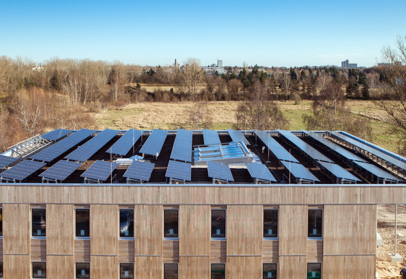 quadratischer zweigeschossiger Bau mit Holzfassade und Solarzellen auf dem Dach