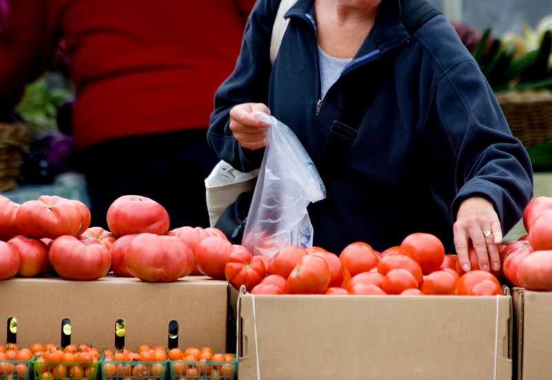 eine Kundin packt an einem Marktstand Tomaten in einen dünnen Plastikbeutel