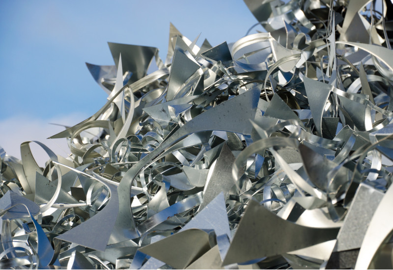 Verschnitt-Stücke aus silbernen Metallblechen liegen auf einem großen Haufen, dahinter ist blauer Himmel zu sehen