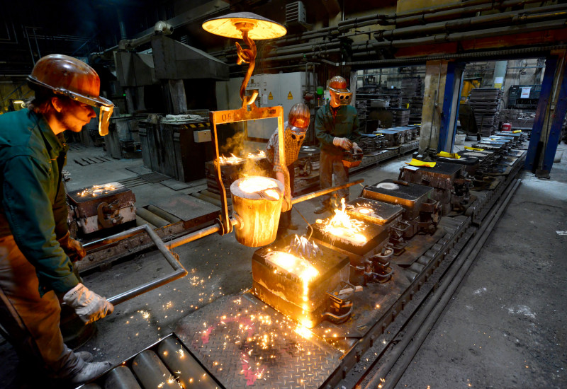 In einer Gießerei gießen Arbeiter flüssiges, glühendheißes Metall in Formen