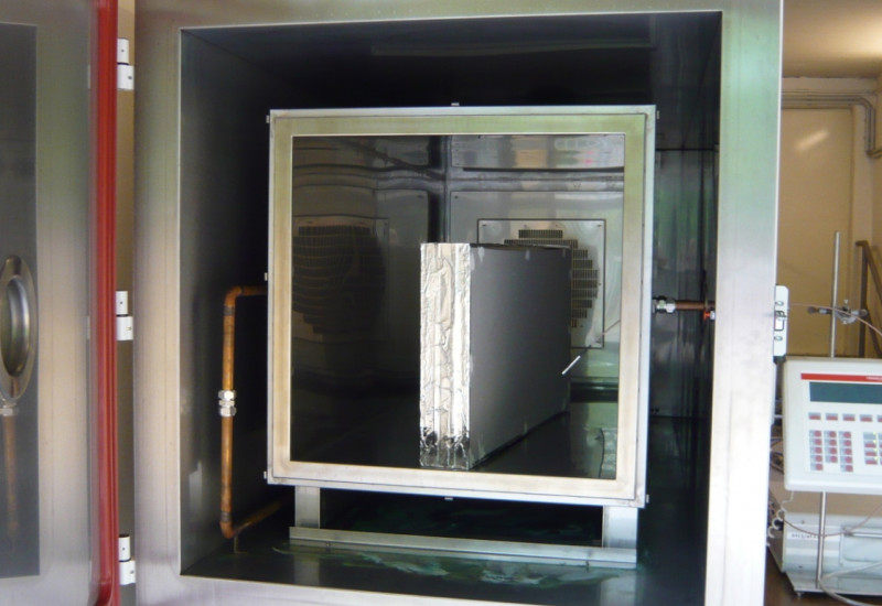 in einem großen Stahlbehälter mit Tür steht ein Bauprodukt, daneben ein elektronische Gerät zur Durchführung einer Emissionsmessung