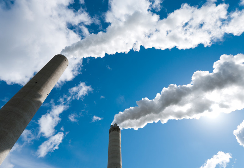 aus Industrieschornsteinen steigt Rauch in blauen Himmel auf