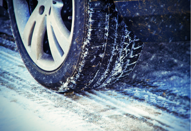 ein Auto fährt bei Schneetreiben über eine verschneite Fahrbahn, Großaufnahme eines Reifens