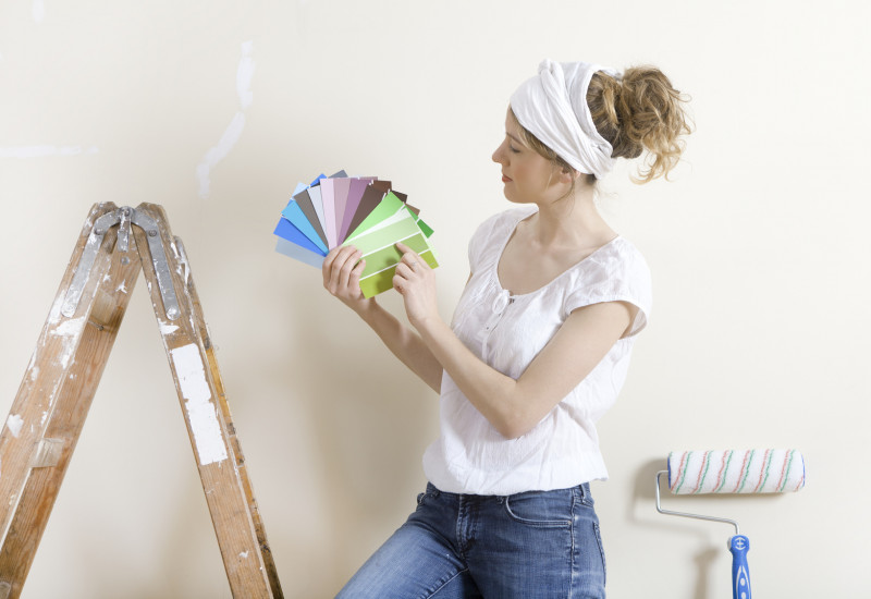 Frau sucht mit einem Farbfächer eine Wandfarbe aus