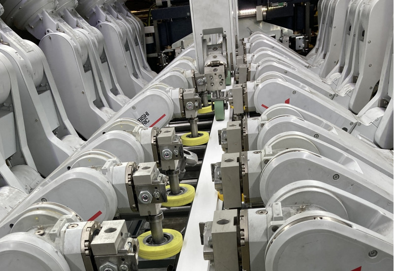 technische Anlage mit 12 Roboterarmen, die eine Folie auf ein PVC-Profil aufbringen