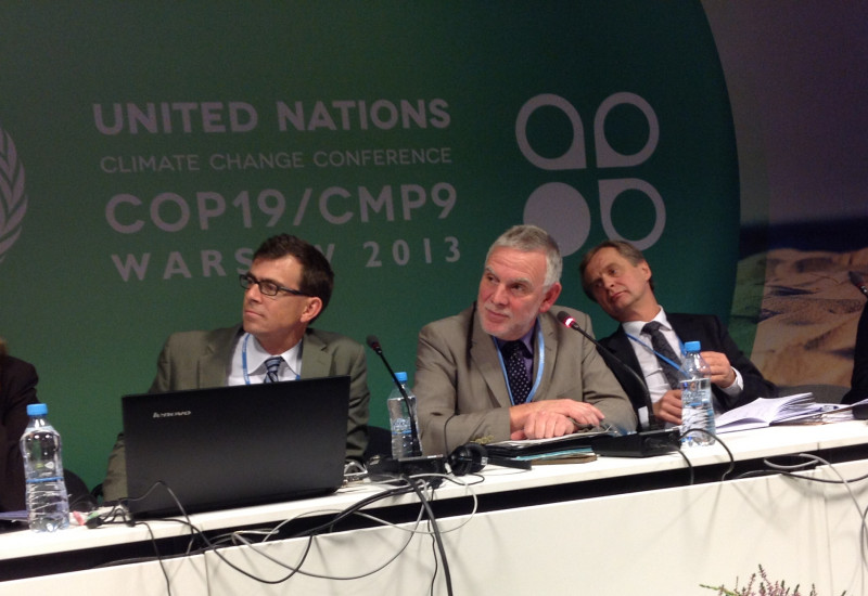 Jochen Flasbarth mit anderen Rednern auf einem Podium, im Hintergrund eine Stellwand mit dem Logo der Warschauerr Klimakonferenz COP19/CMP9