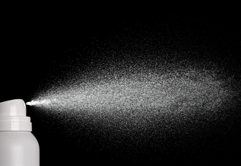 white aerosol can sprays in front of black background
