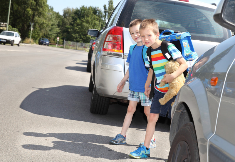 zwei Schulkinder überqueren zwischen parkenden Autos eine Straße