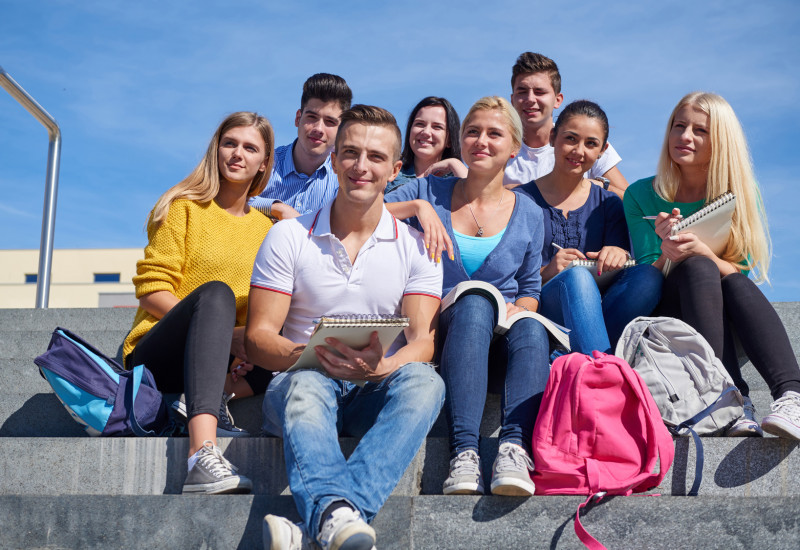 eine Gruppe Studentinnen und Studenten sitzt mit Rucksäcken und Schreibblöcken auf einer Steintreppe