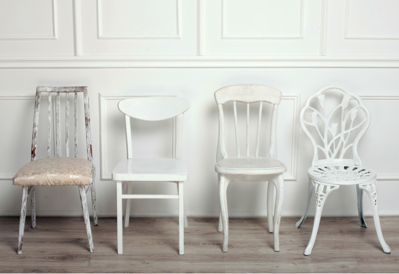 drei weiße Stühle im unterschiedlichen Stil vor einer weiß vertäfelten Wand mit Holzdielenboden