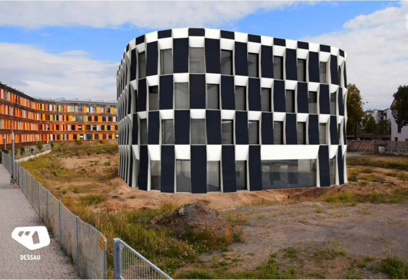 neben dem UBA-Gebäude Dessau-Roßlau ist eine Brache mit Bauzaun. Per Computersimulation wurde der geplante Erweiterungsbau mit seinen großen Photovoltaikelementen an der Fassade, reingesetzt.