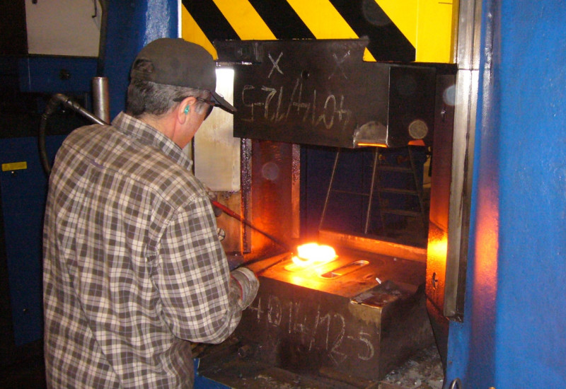 Mann arbeitet an einem glühenden Metallteil in einer Schmiedemaschine