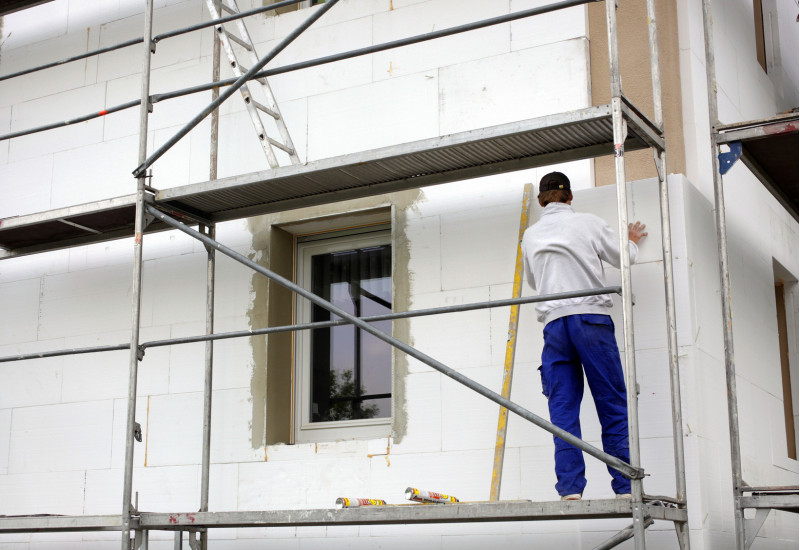 Handwerker steht auf einem Baugerüst und bringt Styroporplatten an eine Hausfassade an