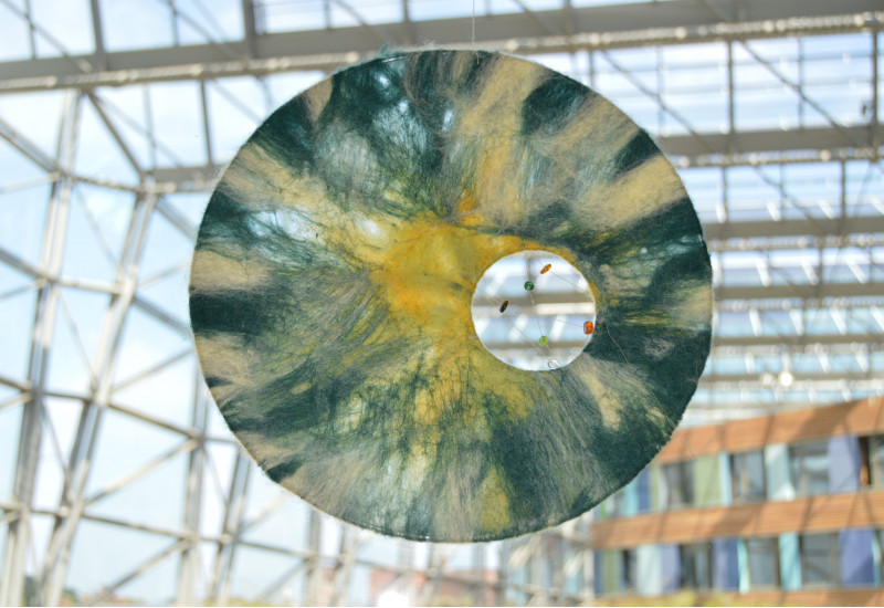 an einer Glasfront des UBA Dessau hängt eine halbtransparente Scheibe, die an Sonne, Mond, Himmel und Wolken erinnert. Ein Guckloch bietet einen Einblick ins Innere des Gebäudes